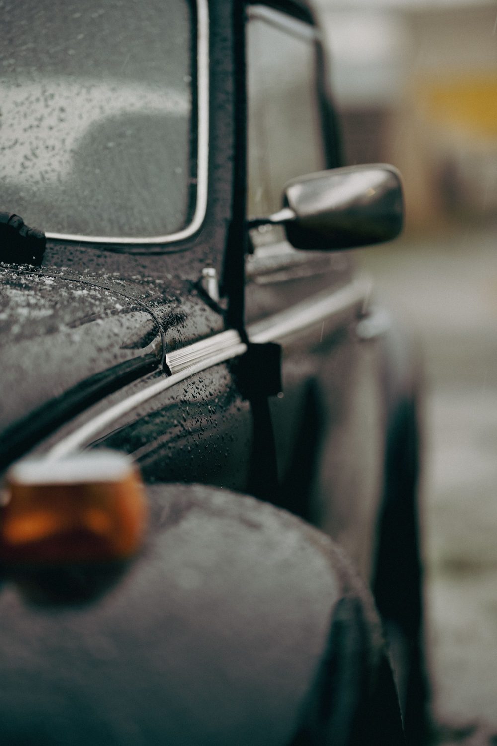 Detailaufnahme eines Fahrzeugs im Regen: Seitenspiegel, Scheibe und orangefarbener Blinker